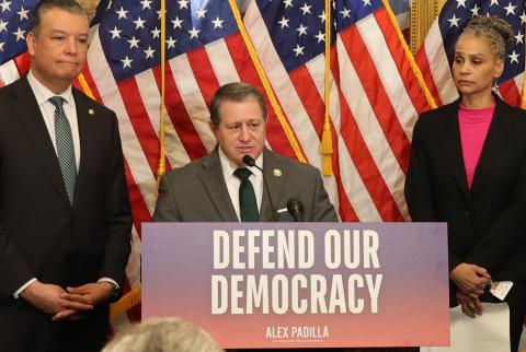 Congressman Morelle stands at a podium speaking with the words "Defend our Democracy" on the podium.
